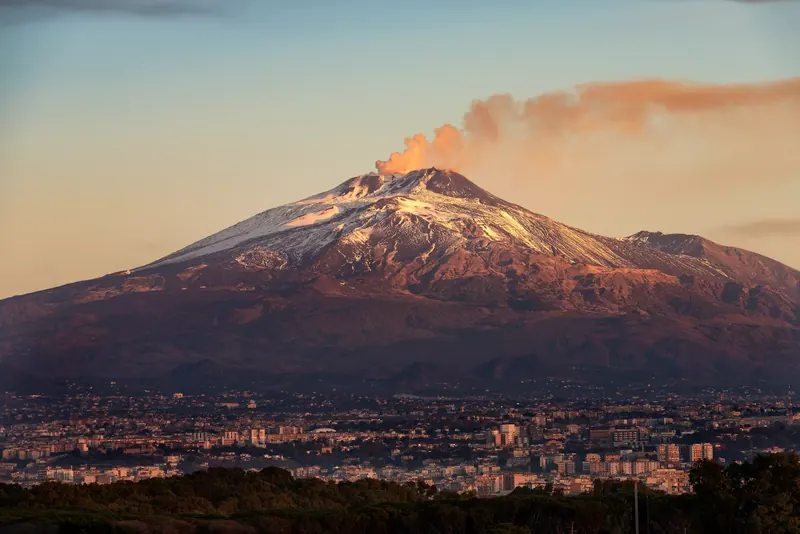 L'Etna innevato con il pennacchio di fumo al tramonto