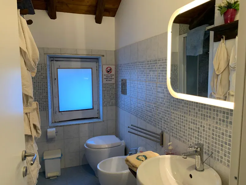 Secondo bagno con mosaico azzurro, specchio illuminato e travi in legno