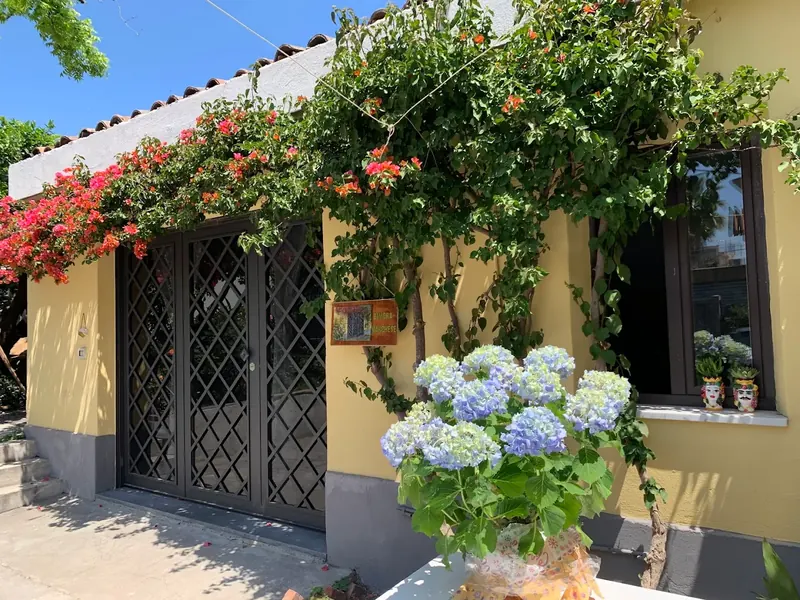 Ingresso della villa: facciata gialla, cancello in ferro, bouganville fiorite e ortensie azzurre