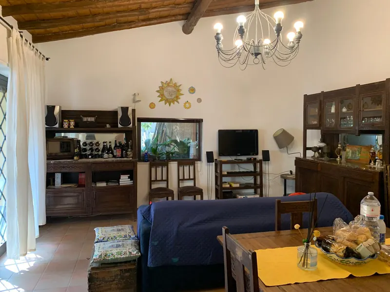Soggiorno con travi in legno, lampadario in ferro e credenze siciliane intagliate